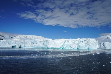 Fototapeta na wymiar Summer landscape in Antarctica with melting snow, sea, icebergs, white clouds.