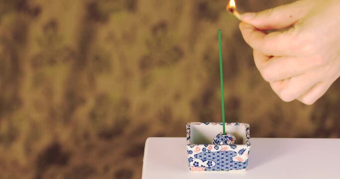 Hand with match light up the joss sticks in incense stand. Incense at home are burning and smelling.