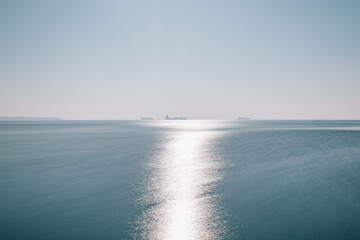 seascape of aegean sea with a faint hazy tanker ship boat in the horizon. blue sky no clouds with blue sea with some small ripple waves sun reflection