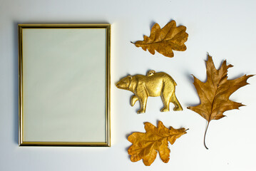 Empty gold frame with gold bear figurine on a white background among autumn leaves. Autumn...