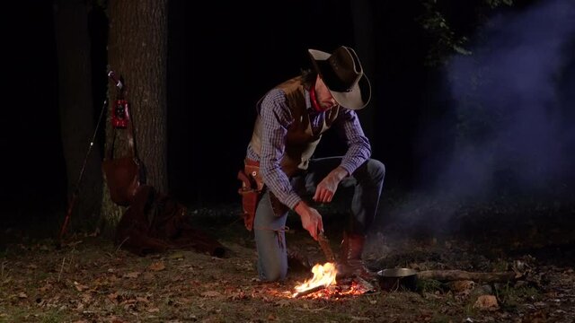 Cowboy near the fire in the forest at night. Historical reconstruction of life in the wild west of America. 4K