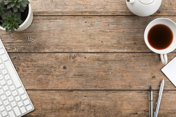 Rustic wooden desk background with teapot, tea cup, sempervivum houseplant, pens and copy space,...