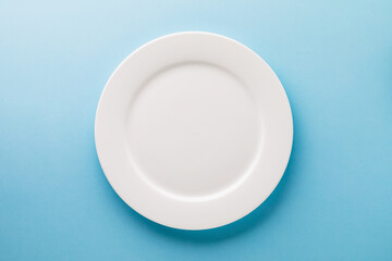 Flat ceramic plate white on a blue background, top view. Food background