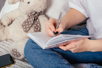 Close-up of hands of a teenage girl writing in a notebook with a pen.Home schooling concept.