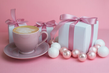 Gift or present box with shiny balls ,coffee, ribbons and snowflakes on pink background. Flat lay composition for christmas, female Christmas. White gift with pink ribbons. A gift box isolated on pink