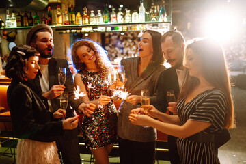 Group of happy people holding sparklers at the party. Young friends clinking glasses of champagne and enjoying new years eve with fireworks. Party, celebration, holidays concept.