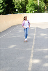 Smiling happy cute little girl child  skating on a skateboard. Preteen riding on a penny board outdoors in summer