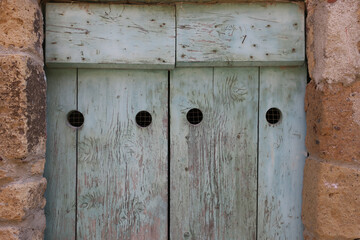 gray painted wooden door with four holes in a stone wall