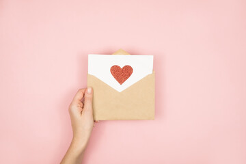 Obraz premium Love letter in women hands on Valentines Day. Handmade postcard with red heart on pink background. 14 February concept