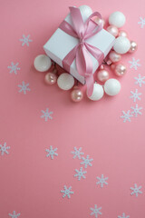 Gift or present box with shiny balls, ribbons and snowflakes on pink background. Flat lay composition for christmas, female Christmas. White gift with pink ribbons. A gift box isolated on pink 