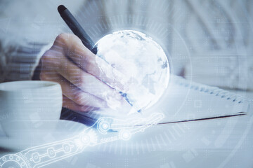 Double exposure of hands making notes with world map hologram and data theme icons. Concept of global computer data.