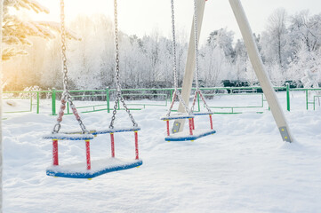 Empty swing in winter with snow. The symbol of the pandemic is the absence of adults and children on the street. Stay at home. Seasonal entertainment