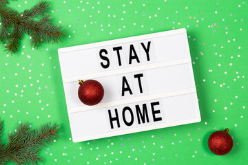 Light box with text STAY AT HOME and Christmas decoration on green background. Top view