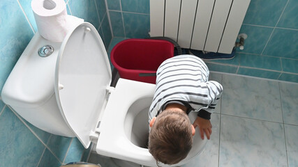 Cute boy in striped clothes washes a toilet. The child cleans at home. Household duties. The idea...