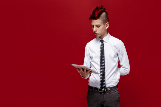 Portrait of red-haired teen punk with tablet against of red background. Isolated.