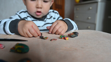 Little boy moulds from plasticine on table, Child hands playing with colorful clay, day care close up, tactility activity.