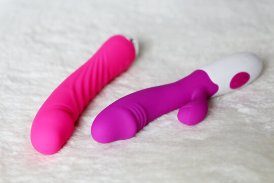 Adult toys on a white fur rug. Two dildo on a bed, pink silicone vibrators