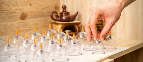 Hand of massage therapist takes vacuum glass jars from a table in a spa