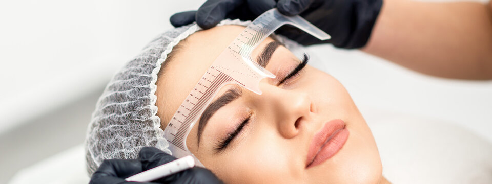 Beautician is measuring the brows with ruler before tattooing eyebrows