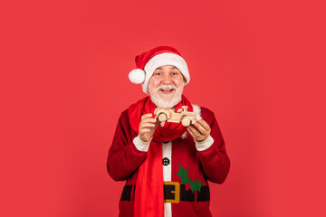 bearded santa with wooden car toy on red background. xmas presents and gift shopping time. winter holiday joy. funny senior man in santa claus costume. happy new 2021 year. merry christmas