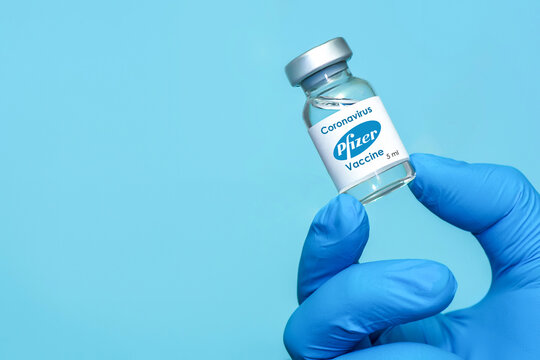 Kharkiv. Ukraine. November 23, 2020. The hand of a doctor or loborant wearing latex gloves holds the Coronavirus vaccine developed in collaboration with Pfizer and BioNTech against a blue background.