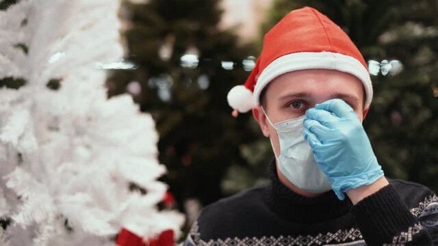 Close up shot of a man in santa hat, medical gloves and christmas sweater puts on medical mask in supermarket. Shopping during pandemic covid-19 coronavirus concept