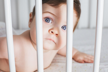 Cute baby boy portrait in a white bed. White nursery for young children. Little boy learning to...