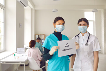 Nurses in protective mask stand with a sign in their hands with the inscription vaccination