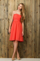 Fototapeta premium beautiful slender blonde girl in a light red dress near a wooden wall