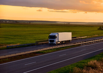 Fototapeta na wymiar Truck with semi-trailer driving along highway on the sunset background. Goods delivery by roads. Services and Transport logistics. Soft focus.