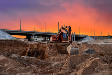 Excavator during excavation at construction site on amazing sunset background. Backhoe on road...
