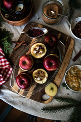 Process of making baked apples. Fresh red apples stuffed with hazelnuts, raisins, lingonberry and brown sugar on wooden board on Christmas table.