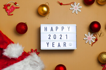 Small interior lightbox with an inscription Happy 2021 Year on a warm yellow background with Christmas decorations and a Santa Claus hat.