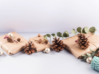 Christmas festive scene with wrapped zero waste presents, golden decor, pine cones and eucaliptus on gray background.