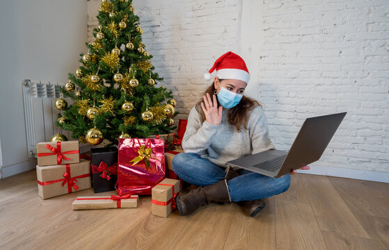 Happy woman in lockdown with face mask on video call celebrating virtual christmas with family
