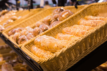 fresh golden breads with melted cheese wrapped in plastic wrap in wicker basket in bread department of supermarket