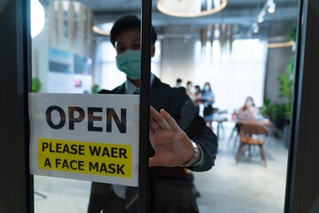 A businessman wearing a surgical mask puts an open sign 