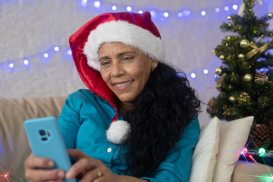 Mature woman with Santa Claus hat using blue cellphone. At home, enjoying the Christmas festivities.