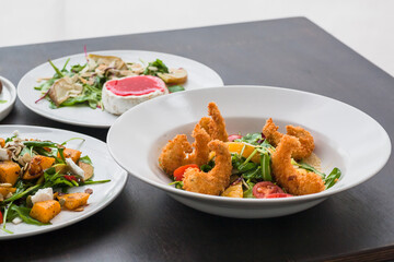 Salad with shrimp in crispy breadcrumbs and othe meals on restaurant table. Fresh food from menu