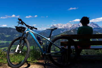 Mountainbikerin macht eine Pause im Schatten mit Blick auf die Berge und in das Tal