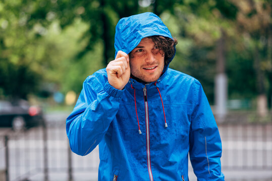 Outdoor image of the man wearing a blue raincoat during rain outside. Male in blue raincoat enjoying the rain in the city street. Man walking in rainy weather.