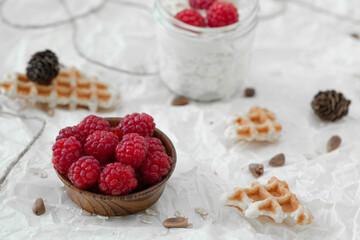 Cottage cheese with raspberries and muesli and waffles, on top of yogurt in a jar wrapped in a white warm sweater.