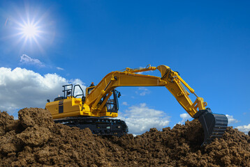 Yellow excavators are digging the soil in the construction site with the sky and sunbeam background