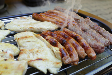 Delicious meat on barbecue grill with steam.Close up.Assorted grilled chicken, kebab, sausages.Small cheap electrical barbecue BBQ grill at home.
