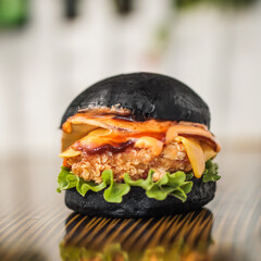 Chicken zinger black bun burger on a table with cheese and vegetables inside placed on a wooden...