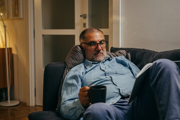 middle aged man relaxed on sofa reading book at home