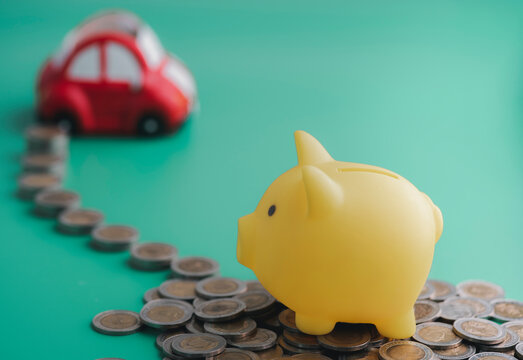 A yellow piggy bank was placed on top of a pile of coins and coins that were lined up towards the car. Money saving ideas