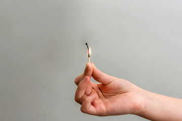 The girl holds a nearly burnt match with her hand on a gray background.