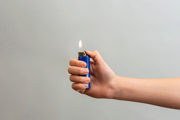 The girl wrapped her hand around the lighter and lit her finger on a gray background. - obrazy, fototapety, plakaty