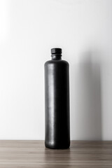 Elegant black clay unlabeled bottle on white background on wooden table.